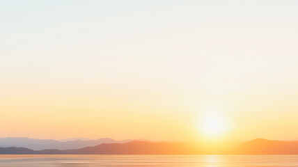 Fototapeta premium Sunrise over calm water with distant mountain silhouettes