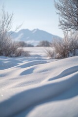 Obraz premium Undulating snow drifts in a frosty winter landscape, mountains in background.