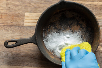Person cleaning a rusty old cast iron fying pan using bicarbonate of soda and a scouring pad. On a...