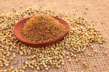 Powdered coriander (Coriandrum sativum) in a wooden bowl and some coriander seeds scattered around it, close up view.