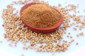 Powdered coriander (Coriandrum sativum) in a wooden bowl and some coriander seeds scattered around it, close up view.