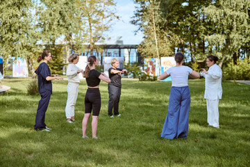 Fototapeta premium Adults of diverse ethnicities practicing qigong in sunny park. Serene expressions, relaxed postures in grassy area. Bright daylight enhances focus