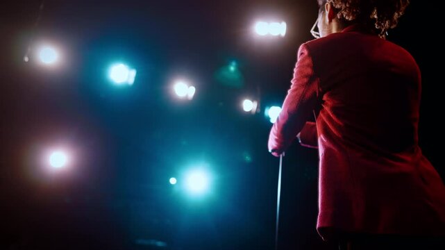Stylish black man with dreadlocks performing on stage of concert hall, back view . Stand-up comedian or host of event, presentation of new business project on conference, back view of african man