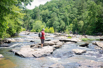 Man exploring a rocky river surrounded by lush greenery and forest © Cavan