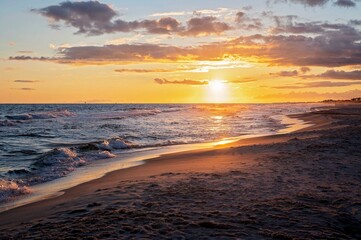 Obraz premium Stunning sunset over a sandy beach with waves gently reaching shore