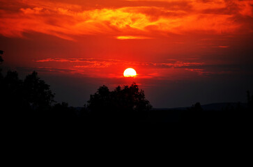 Fiery red sunset over silhouetted trees with a dramatic sky