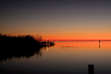 Obraz premium Tranquil sunset over a calm lake with reflections and a wooden dock