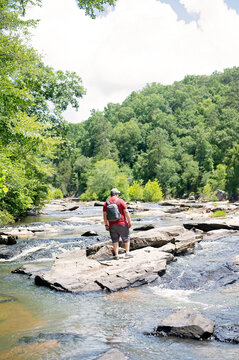 Man hiking along a rocky river in a lush, green forest landscape