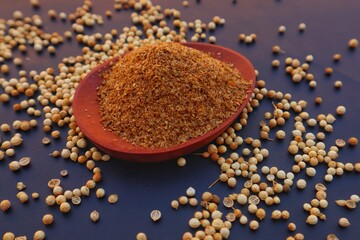 Powdered coriander or Coriandrum sativum in a wooden bowl and coriander seeds scattered around it, close up view.