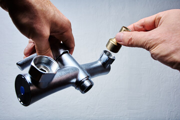 Hands attach brass eccentric reducer to plumbing fixture of . bathroom mixer tap with threaded...
