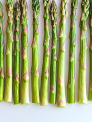 Fototapeta premium A row of fresh, vibrant green asparagus stems on a clean white surface, ready to be prepared in your kitchen.