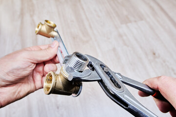 Wrench is tightening stainless steel threaded nipple wrapped in plumbing flax into brass fitting...