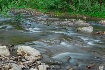 Silky smooth river water flows over rocks in a peaceful landscape on a sunny day.
