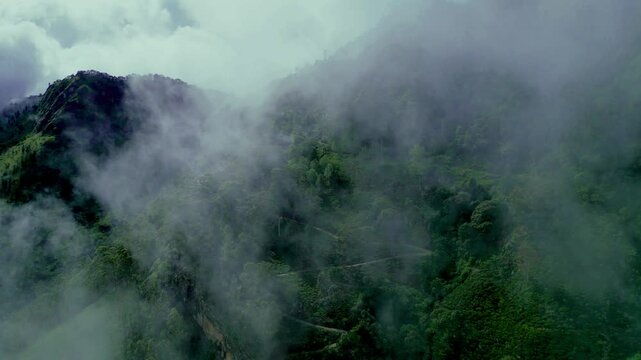 Drone glides through mist, revealing winding mountain roads and lush green peaks in Sri Lanka