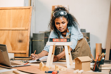 African American carpenter woman uses a level on a wooden stool in the workshop. Master joiner...