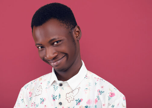 Close-up headshot of a young man in a floral shirt making a weird, awkward smile against a coral background. His playful and humorous expression adds a quirky and lighthearted feel to the portrait.