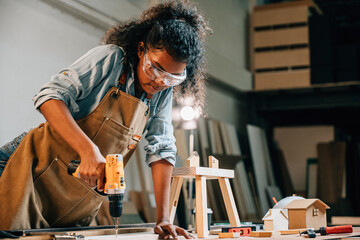 Carpenter woman using a power drill to secure a piece of wood in a workshop, focusing on precision...