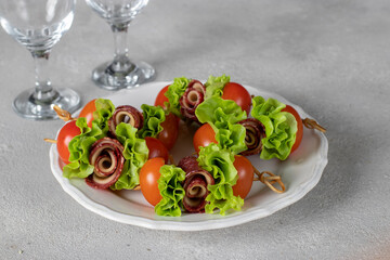 Canape with sausage, cheese, cherry tomatoes and lettuce leaves on white plate, festive snack