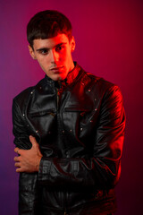 Obraz premium Young man wearing black leather jacket posing under red and purple lights