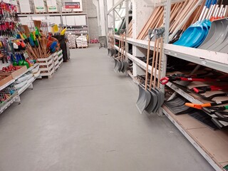 An aisle in a hardware store displaying various shovels, brooms, and gardening tools on shelves