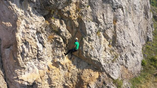 Aerial view of mountain rescuer rappelling on a rocky wall hanging on a rope