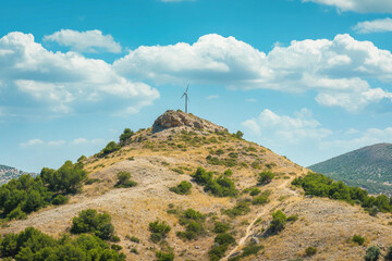 Fototapeta premium Scenic Hilltop Wind Turbine under a Bright Sunny Sky with Fluffy Clouds and Lush Green Vegetation