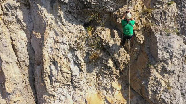 Aerial view of mountain rescuer rappelling on a rocky wall hanging on a rope