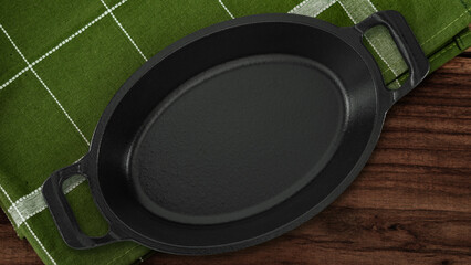 Black cast iron oval skillet placed on a green checkered napkin over a rustic wooden table, ideal...