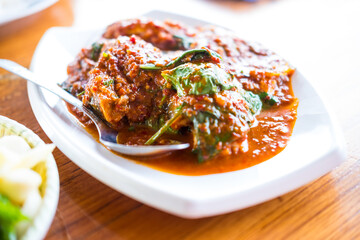 Fried fish with red curry paste served on white bowl on wood table