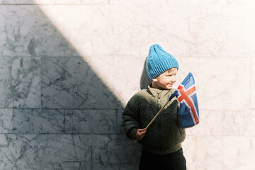 Young boy holding icelandic flag in front of marble wall