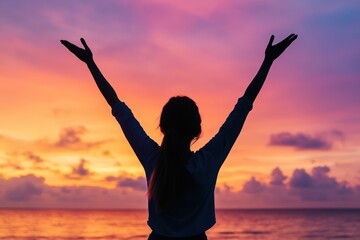 Silhouette of woman with outstretched arms at vibrant sunset by the sea