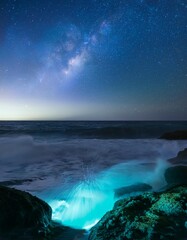 Exploring the Mystical Beauty of Bioluminescent Waves Crashing Against a Rocky Shoreline Under a Starry Night Sky