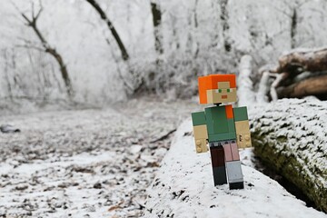 Fototapeta premium LEGO Minecraft action figure of female character Alex walking on chopped down tree logs in heavily frozen winter forest. 