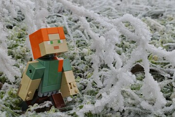 Naklejka premium LEGO Minecraft figure of Alex adoring heavy icing on winter tree branches, frozen grass in background. 