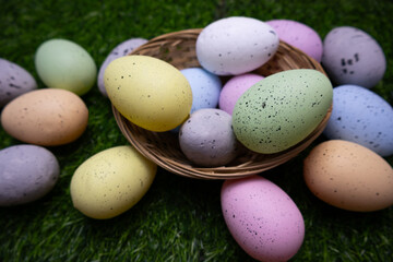 Easter background of pastel colorful eggs in a twigs basket on grass