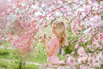 beautiful blonde young woman in a blooming spring garden. A girl on a background of pink cherry blossoms enjoys the fragrance