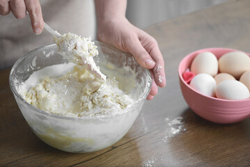 a woman kneads the pasta dough in a transparent plate on the table with her hands