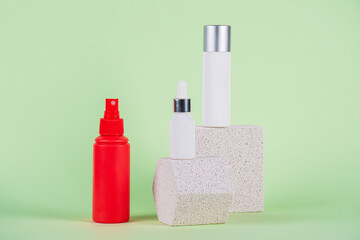 White tube and red spray on light white podiums. White blank unbranded flacons with cosmetology products. Professional concept of skin care on green background.
