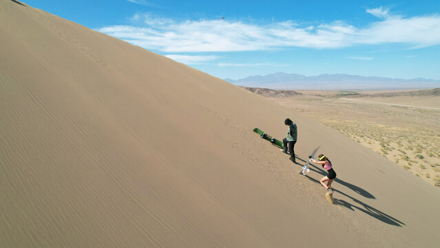 Two sandboarders preparing to descend a large sand dune in the lut desert, a unesco world heritage site located in kerman province, southeastern iran