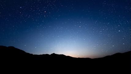 A movement of stars in the night sky with the view of mountains..