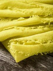 Closeup Detailfoto eines liegenden gelben Cashmere Tuch Schal mit Fransen auf Holz Untergrund