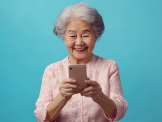 Happy Elderly Woman in Pink Lace Blouse Using Smartphone on Blue Background