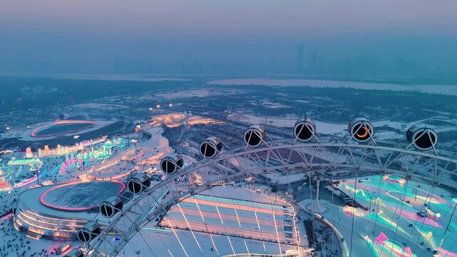 Slow aerial shot of snowflake Ferris wheel at sunset at Harbin Ice Festival with the city's skyline in the background, China