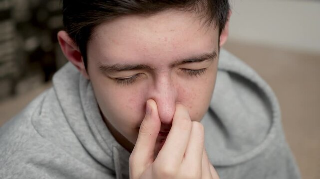 Teenage boy picks and scratches nose with finger. Adolescent male uses finger to scratch and touch nose. Young guy rubs and picks nose with finger