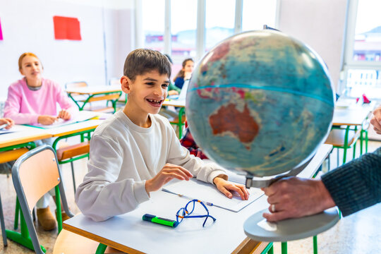 Teacher showing globe to students during geography lesson in classroom