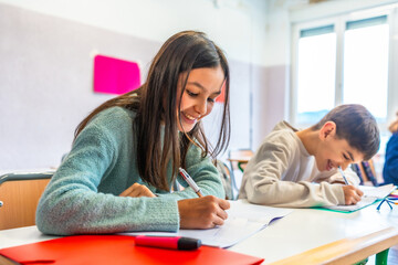Fototapeta premium Elementary school students writing and smiling in class
