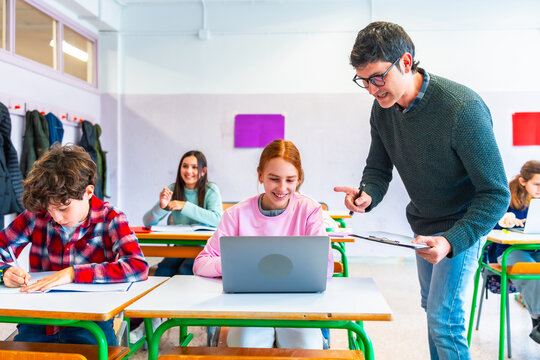 Teacher helping student using laptop in classroom during lesson - Powered by Adobe