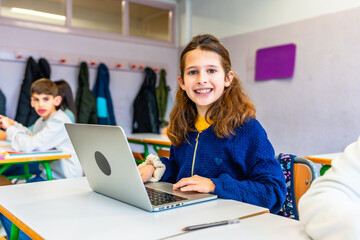 Smiling student using laptop in classroom at elementary school