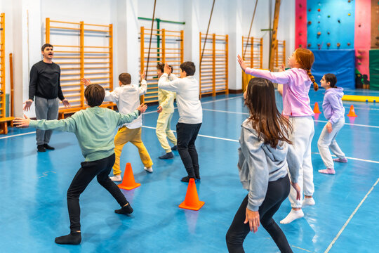 Group of elementary school students doing gymnastics exercises in gym class with teacher