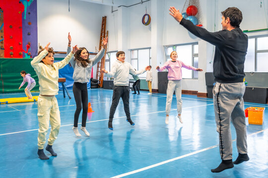Group of elementary school students jumping together with teacher in gym class